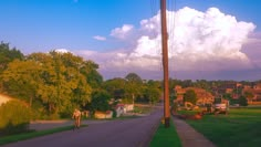 a person riding a bike down a street next to a lush green field and houses