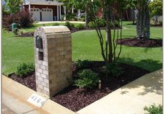 a brick mailbox sitting in the middle of a flower bed next to a tree