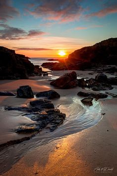 the sun is setting over some rocks on the beach