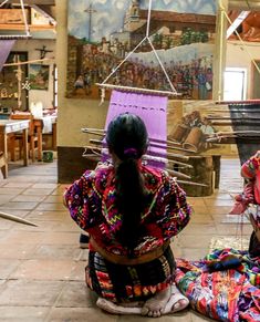 two women sitting on the floor in front of some weaving machines and rugs,