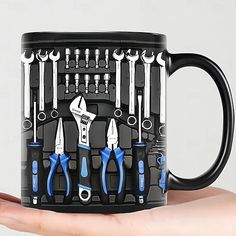 a hand holding a black coffee mug with blue handles and various tools on the inside