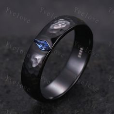 a wedding ring with a blue diamond in the center on a black surface, against a dark background