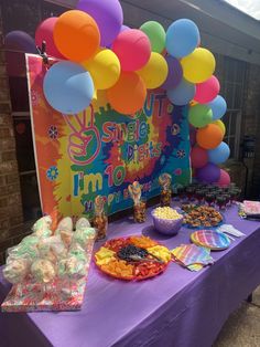 a purple table topped with lots of candy and balloons