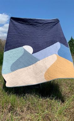 a quilted blanket sitting on top of a wooden bench in the middle of a field