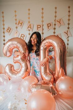 a woman standing in front of balloons that spell out the number twenty five, surrounded by pink and gold balloons