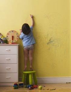 a young child standing on top of a stool in front of a wall with the words kid - proof home design written on it