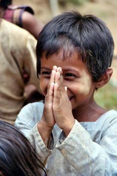 a young boy is smiling and holding his hands together