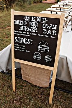 a chalkboard sign sitting on top of a grass covered field next to a table