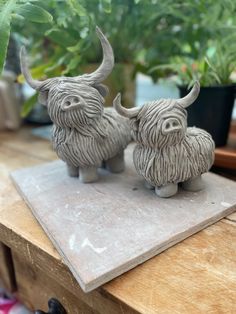 two ceramic bulls sitting on top of a wooden table next to some potted plants