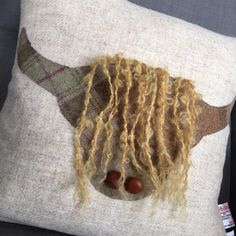 an animal made out of wool and yarn on top of a white pillow with long blonde hair