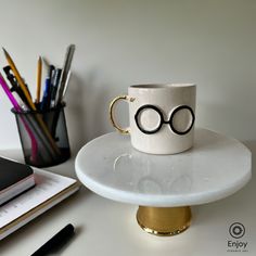 A whimsical ceramic mug featuring black glasses and a gold handle, set on a desk next to stationery, evoking a magical, studious vibe. Glasses Design, Round Glasses, Gold Handles, Handcrafted Ceramics, Hot Beverages, Harry Potter Fan, The Conjuring, Favorite Drinks, Gold Details