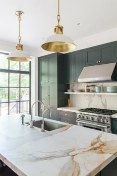 a large kitchen with marble counter tops and stainless steel appliances, along with two pendant lights hanging from the ceiling