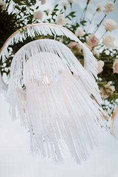 an angel mobile hanging from a tree filled with white flowers and greenery in front of a cloudy blue sky