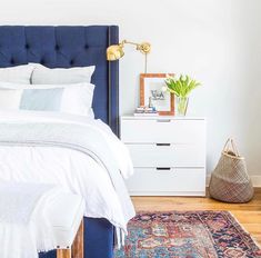 a bedroom with a blue headboard and white linens on the bed, next to a rug