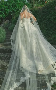 a woman in a wedding dress is walking down some steps with her veil over her head