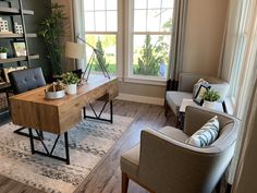 a living room with two chairs and a desk in front of a window that has plants on it