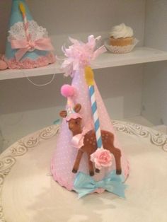 a pink and blue birthday cake with a deer decoration on it's head, next to a cupcake