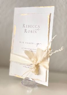 a white wedding card with a bow on the front and back of it, sitting on a table