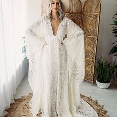 a woman standing in front of a wicker chair wearing a white dress with long sleeves