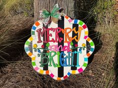 a sign that says merry and bright on the side of a tree in front of some grass