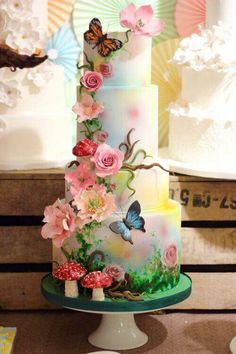 a multi layer cake with flowers and butterflies on it's side, sitting on a table