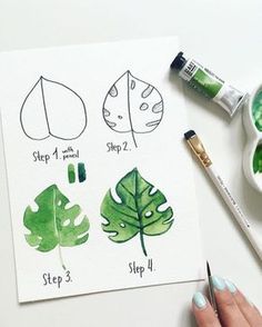 a person holding a paintbrush next to some watercolor paints and a paper with leaves on it