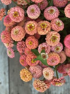 pink and yellow flowers in a vase on a wooden surface with green leaves around them