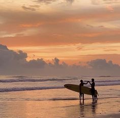 two people standing on the beach with a surfboard in their hands, and one person holding onto another man's hand