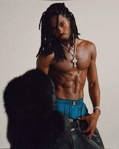 a man with dreadlocks standing next to a black fur ball and wearing blue shorts