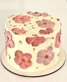 a white cake with pink flowers and gold sprinkles on the top layer