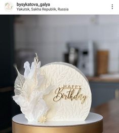 a birthday cake with white flowers on it and the words happy birthday written in gold