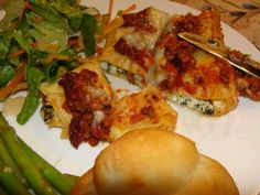 a white plate topped with lasagna and asparagus next to a roll