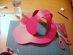 someone is cutting out some pink paper on a table with scissors and other crafting supplies