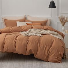 a bed with an orange comforter and pillows on top of it in a white room