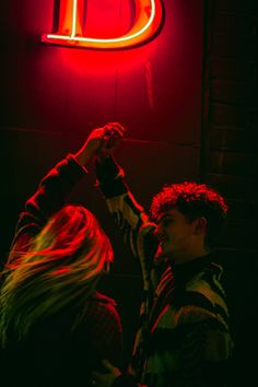 two people standing next to each other in front of a neon sign that reads d