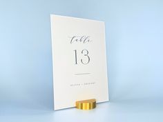 a table number card with a gold ring on it's stand against a blue background