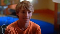 a young man with blonde hair sitting in front of a blue and yellow ball pit