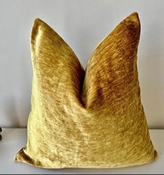 a gold colored pillow sitting on top of a white table next to a black vase