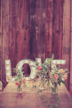 two vases filled with flowers sit on a table in front of a wooden wall