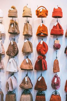 many hats and purses are hanging up on the wall with tags attached to them