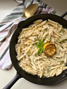 a pan filled with pasta and vegetables on top of a table next to a spoon