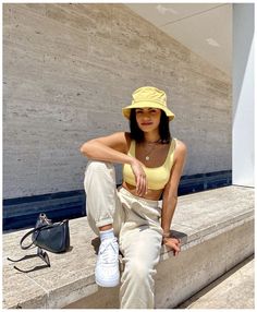 a woman sitting on some steps wearing a yellow hat and white pants with her legs crossed