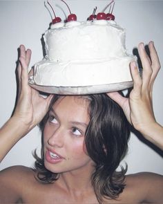 a woman holding a cake on top of her head with cherries on the top