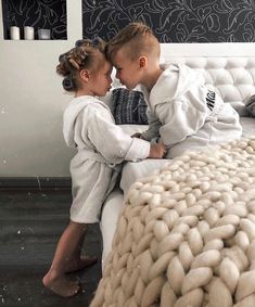 two children are sitting on a bed and one is touching the other's forehead