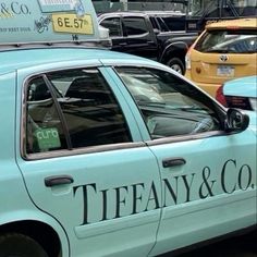 a blue taxi cab parked in front of a parking lot filled with lots of cars