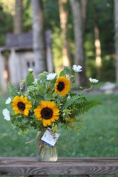 a vase filled with sunflowers on top of a wooden table in the grass