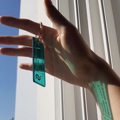 a person's hand holding onto a green keychain in front of a window