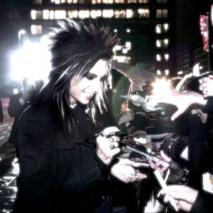 a woman with black hair and piercings signing autographs for people on the street