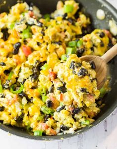 a skillet filled with mexican rice and black beans, topped with a wooden spoon