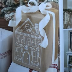 a gift wrapped in brown paper with a gingerbread house drawn on it and white ribbon